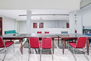 A conference room with a large table and red chairs, white walls, and a green sofa in the background. - OYO 90487 Wisma Kuta Karang Baru (Lhokseumawe)