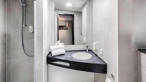 Een moderne badkamer met grijze tegels, een zwart aanrechtbakje, een handdouche en een spiegel.