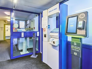 A self-check-in kiosk with a digital screen, a payment terminal, and a sign indicating a check-in point. - Ibis Budget Hannover Messe (Laatzen)
