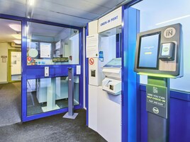 A self-check-in kiosk with a digital screen, a payment terminal, and a sign indicating a check-in point.