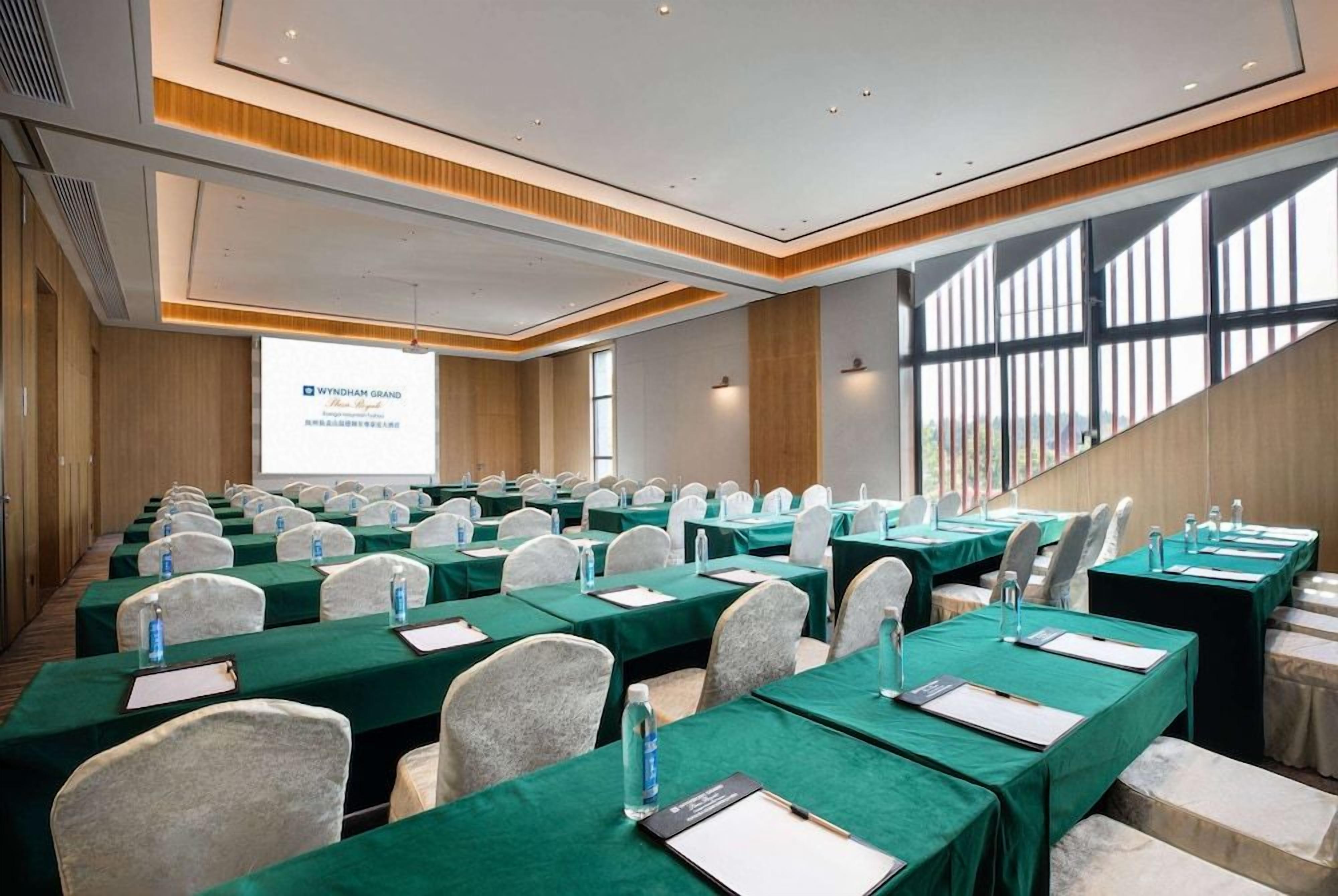 A conference room with rows of tables, chairs, and a projection screen displaying 'WYNDHAM GRAND'.