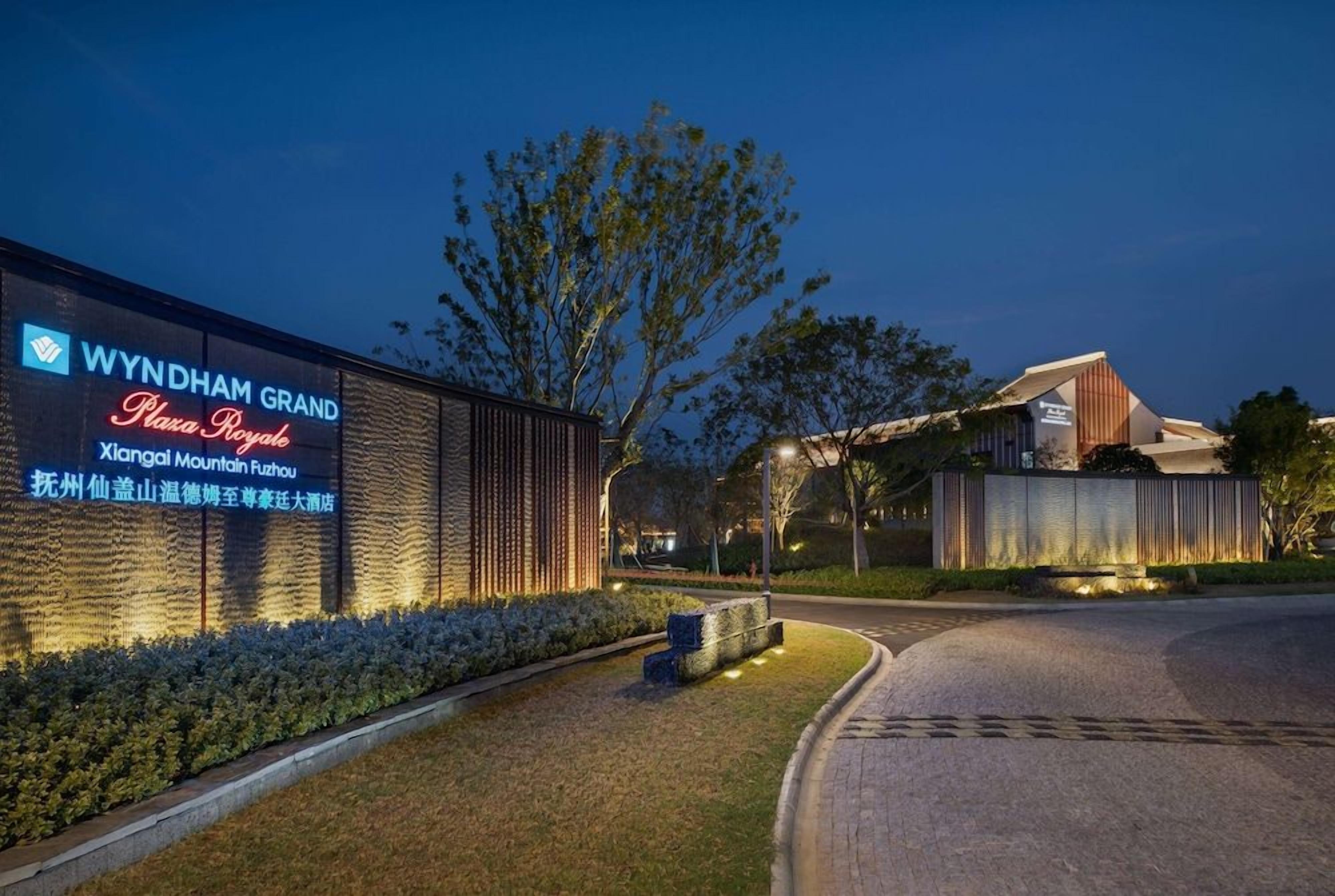 A hotel entrance with a signboard, a landscaped area, and a building structure.