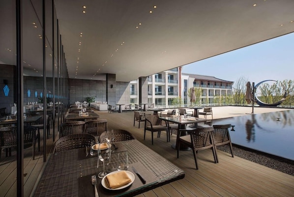 Un espace extérieur aménagé pour les repas, avec des tables et des chaises, une piscine et un bâtiment en arrière-plan.