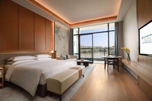 Habitación de hotel moderna con una cama grande, zona de estar, mesa de comedor y un ventanal con vistas.