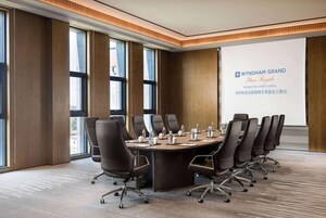Un salón de conferencias con una larga mesa, varias sillas y una pantalla de proyección mostrando información del hotel.