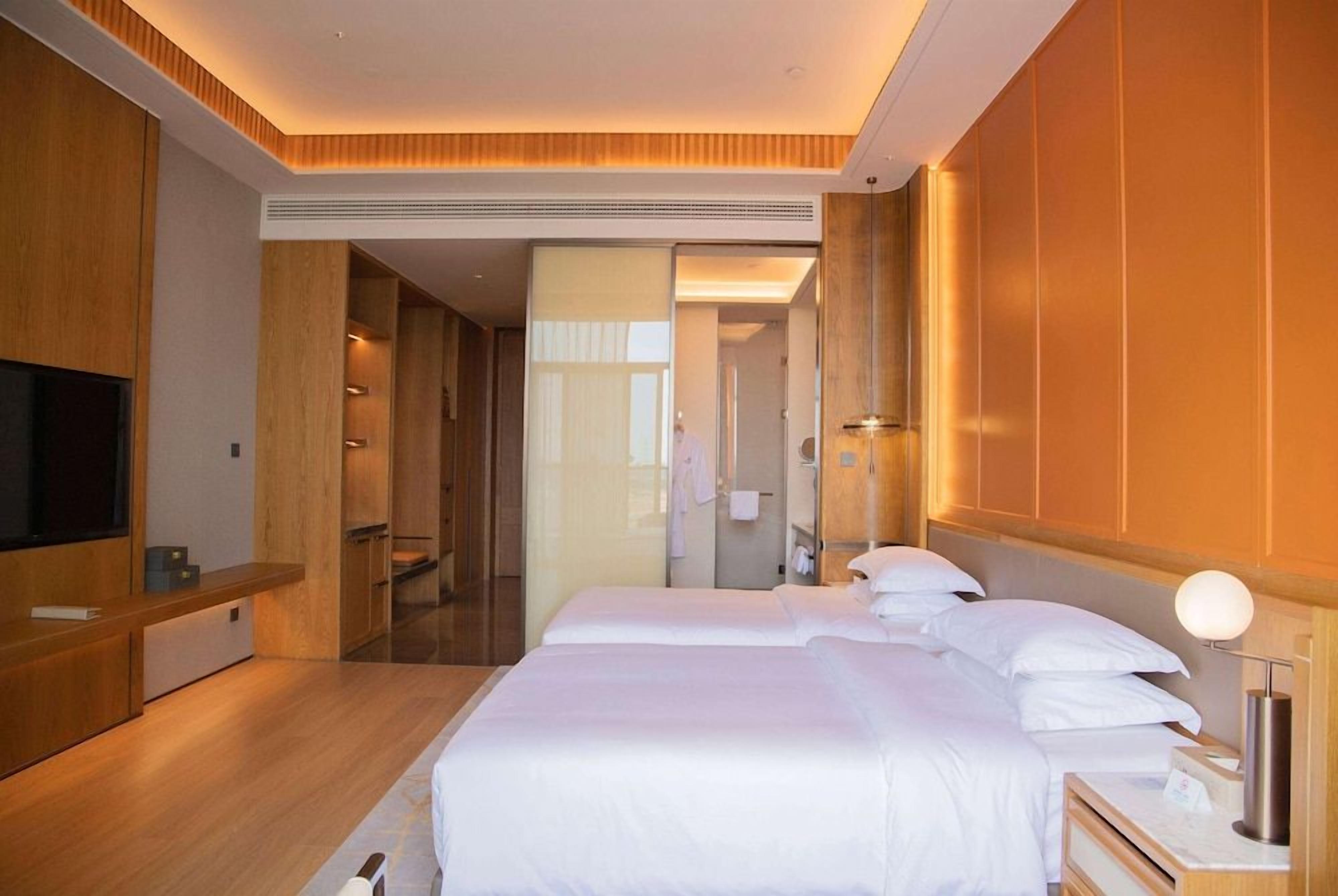 A hotel room with a large bed, bedside tables, a TV, and a bathroom visible through an open door.