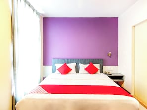 Een hotelkamer met een bed, een nachtkastje en een muur met een lichtschakelaar.