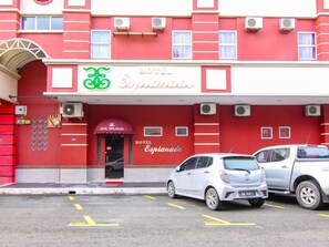 Un edificio rojo con un letrero que dice 'Hotel Esplanade' y un símbolo de bicicleta. Hay dos coches estacionados adelante.