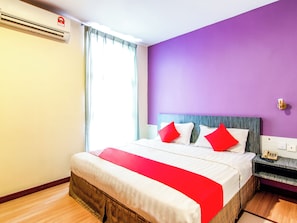Una habitación de hotel con una cama, un teléfono en la mesita de noche y un ventanal con cortinas.
