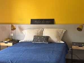 Een slaapkamer met een bed, kussens, een nachtkastje, een lamp en een bord aan de muur.