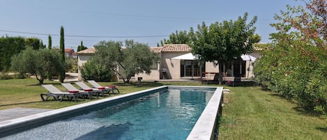 Una piscina con sillas de descanso, un porche techado y un edificio con tejado de azulejos.