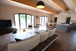 A spacious living area with a sofa, dining table, and chairs, large windows, and a kitchen area. - 8-person Ventoux view villa in the heart of the vineyards (Caromb)