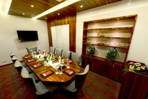 A conference room with a long table, chairs, a flat-screen TV, and a decorative shelf with artificial flowers. - Surestay Hotel By Best Western Model Town Amritsar (Tarn Taran)