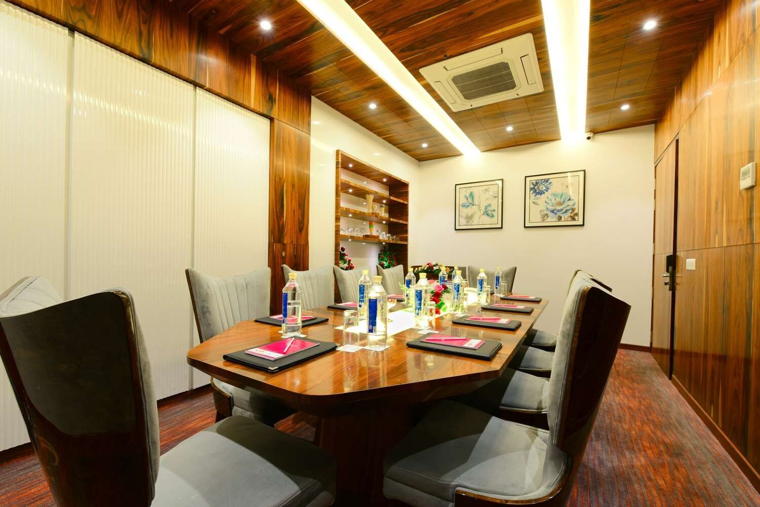 A conference room with a wooden table, grey chairs, water bottles, and a bookshelf.