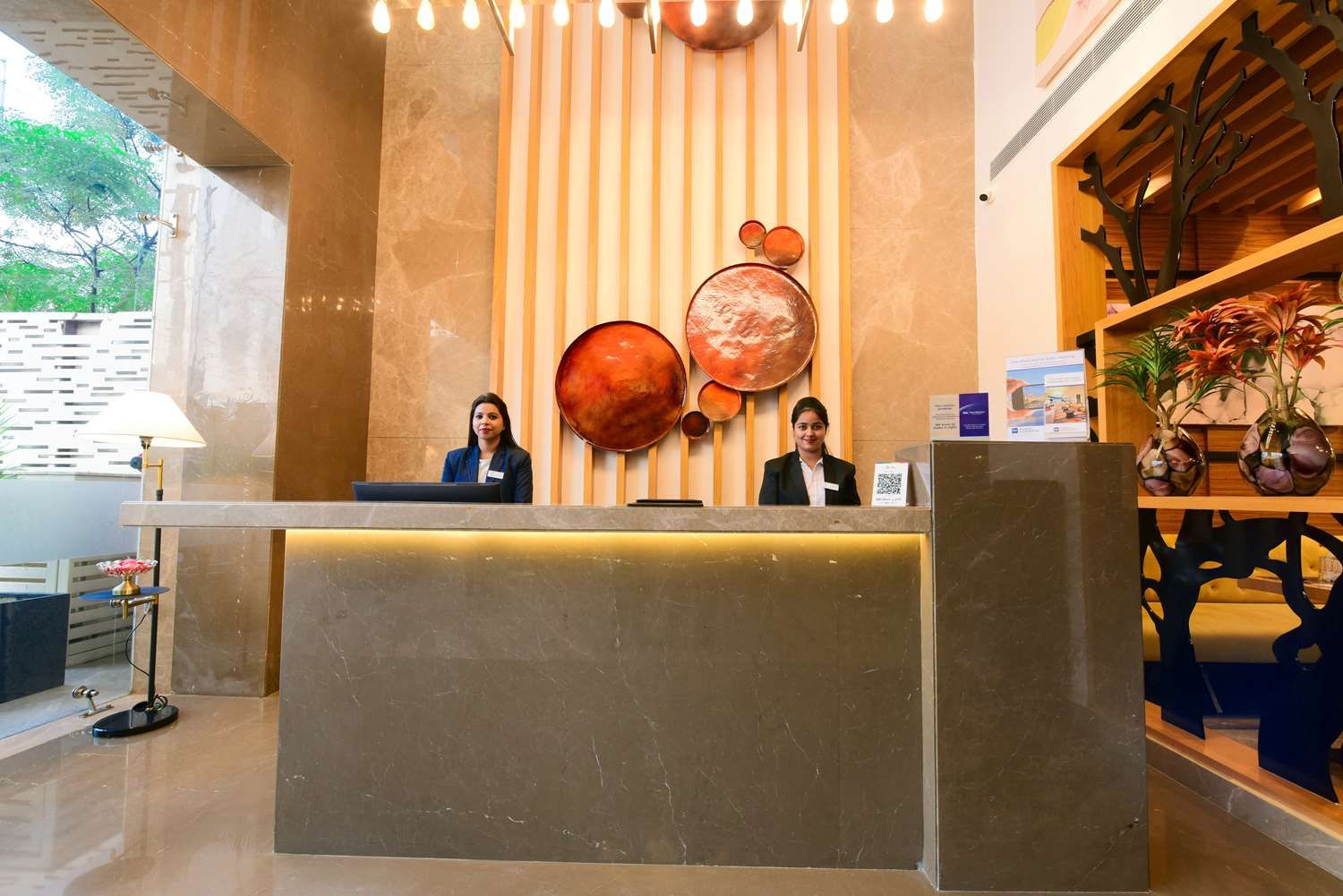 Un comptoir d’accueil avec deux employés, un mur à rayures verticales et une étagère ornée d’objets décoratifs.
