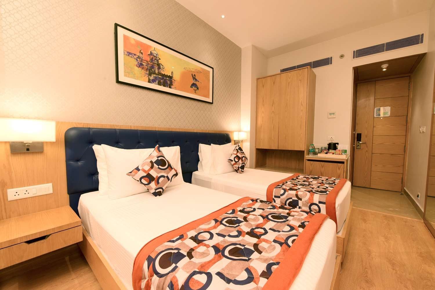 A hotel room with two beds, a headboard, bedside tables, a painting, and a wardrobe.