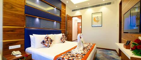 A hotel room with a large bed, a wooden headboard, a flat-screen TV, and a desk with a telephone and a vase of flowers.