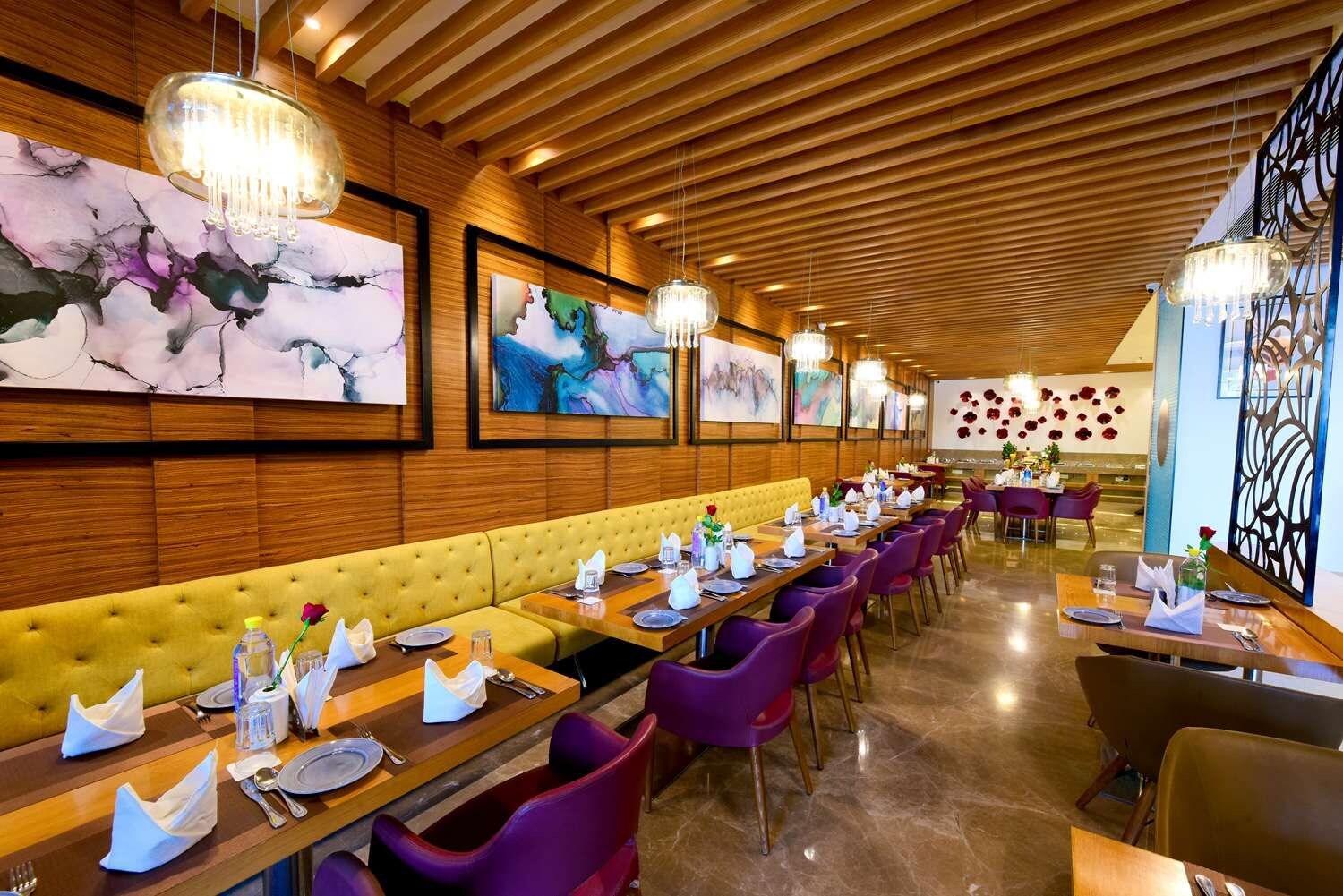 A restaurant with wooden paneling, a yellow cushioned bench, purple chairs, and artwork on the walls.