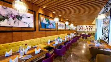 A restaurant with wooden paneling, a yellow cushioned bench, purple chairs, and artwork on the walls.