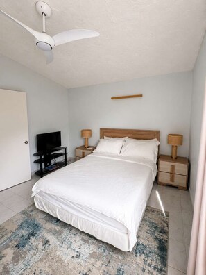 Une chambre à coucher avec un lit, un ventilateur de plafond, un téléviseur et des lampes de chevet.