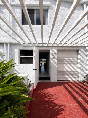 Une entrée d’immeuble avec un chemin en briques rouges, une porte de garage fermée et une enseigne indiquant « Marik’s Jolly Villa 402 D ».