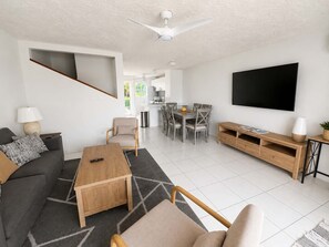 Un salon moderne comprenant un canapé, une table basse, un téléviseur et un coin repas avec des chaises et une table.