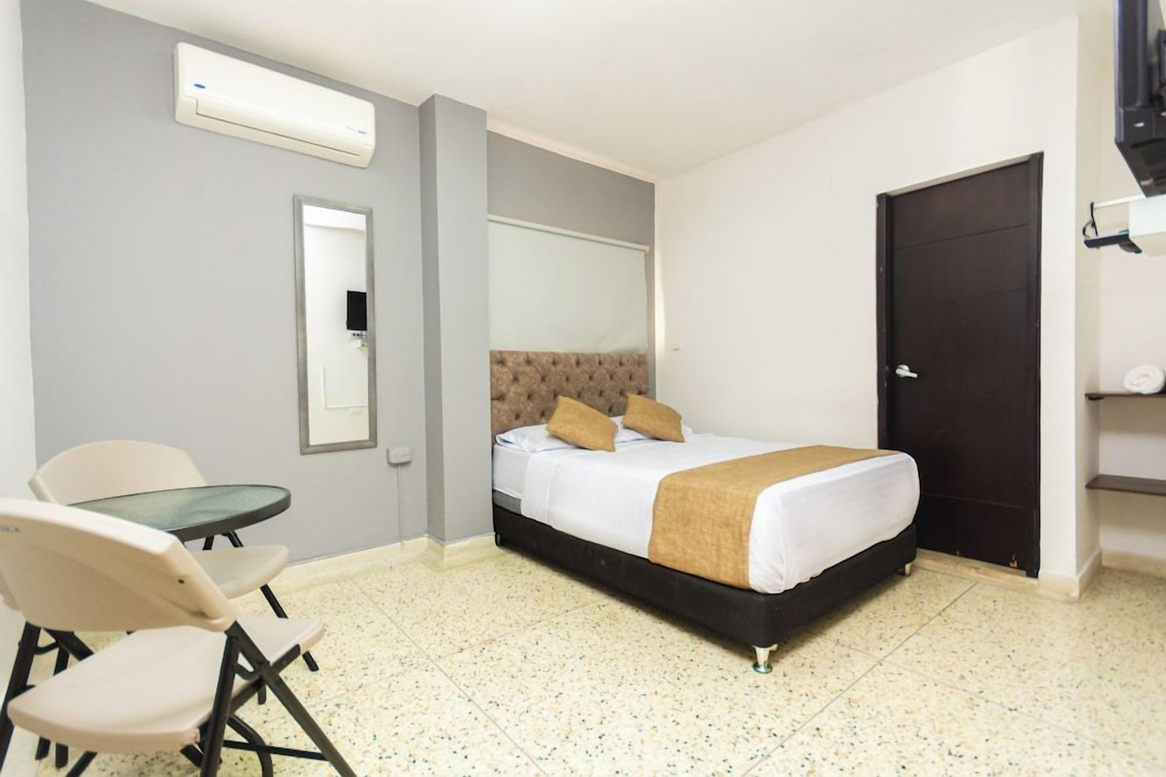 A hotel room with a bed, a small table, two chairs, a mirror, and a door.