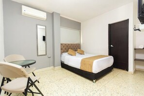 Hotellihuone, jossa on sänky, pieni pöytä, kaksi tuolia, peili ja ovi.