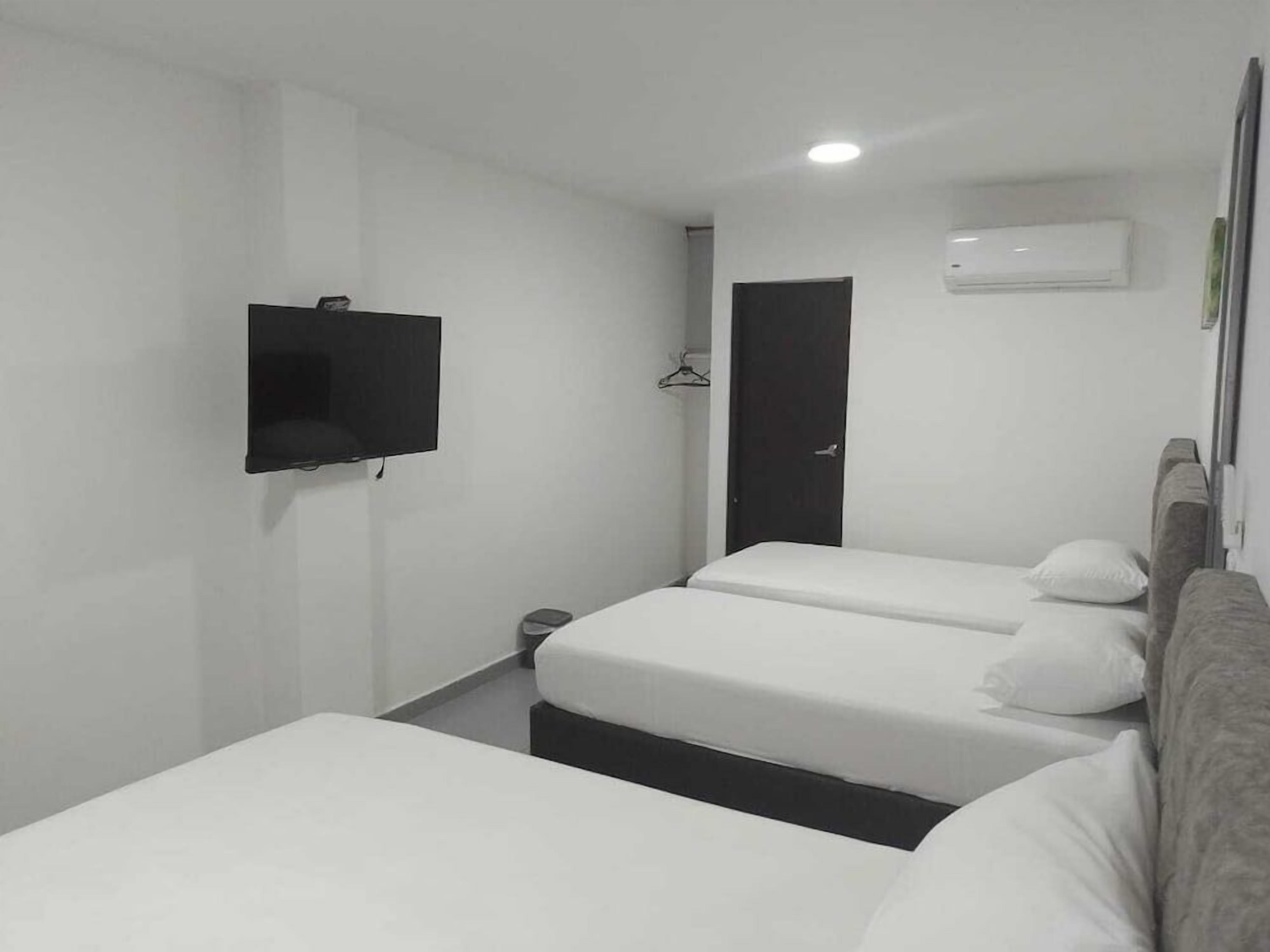 A hotel room with a flat-screen TV mounted on the wall, a door, and a bed with white bedding.