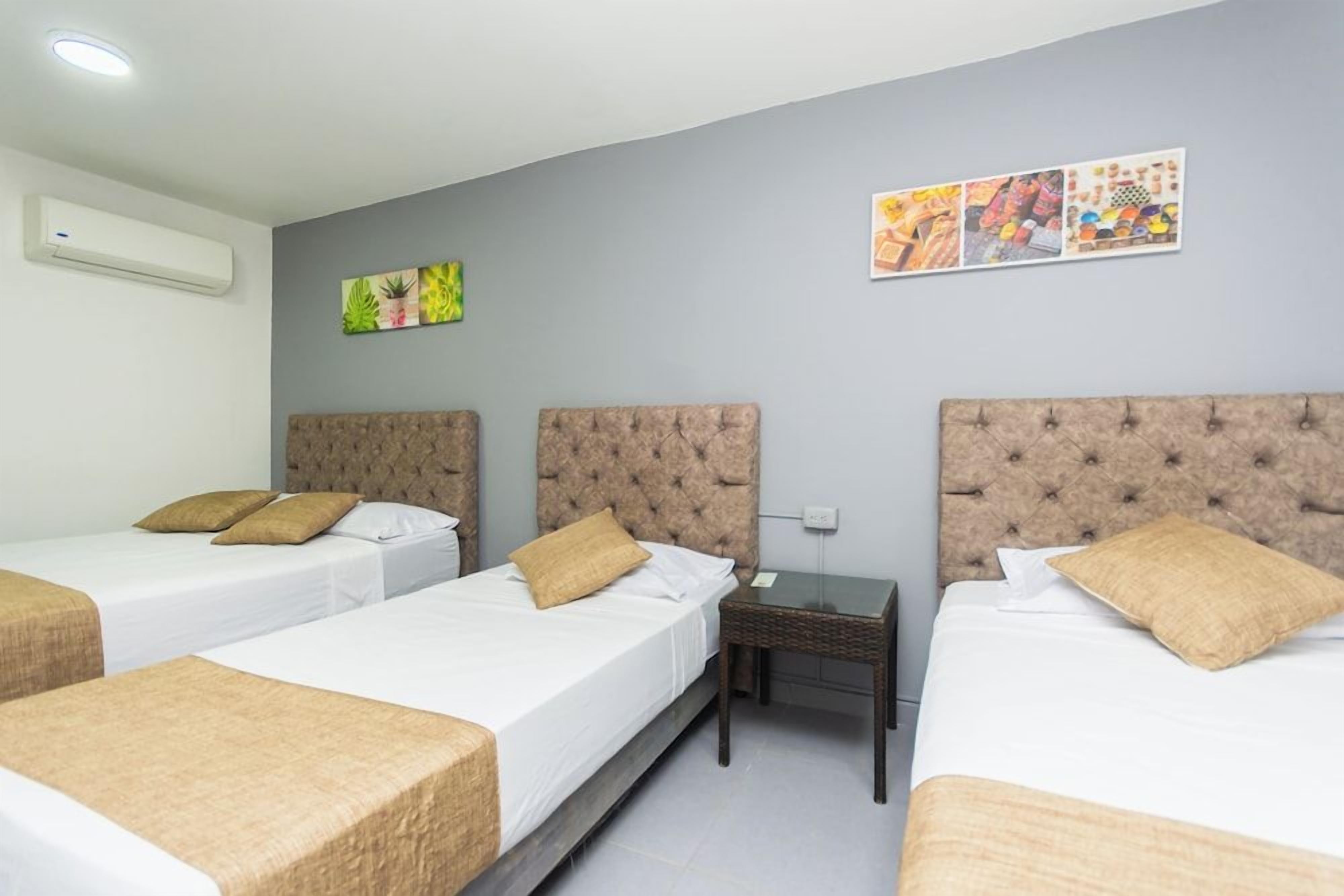 Une chambre d’hôtel avec trois lits, chacun doté d’une tête de lit capitonnée, d’une petite table et d’un climatiseur fixé au mur.