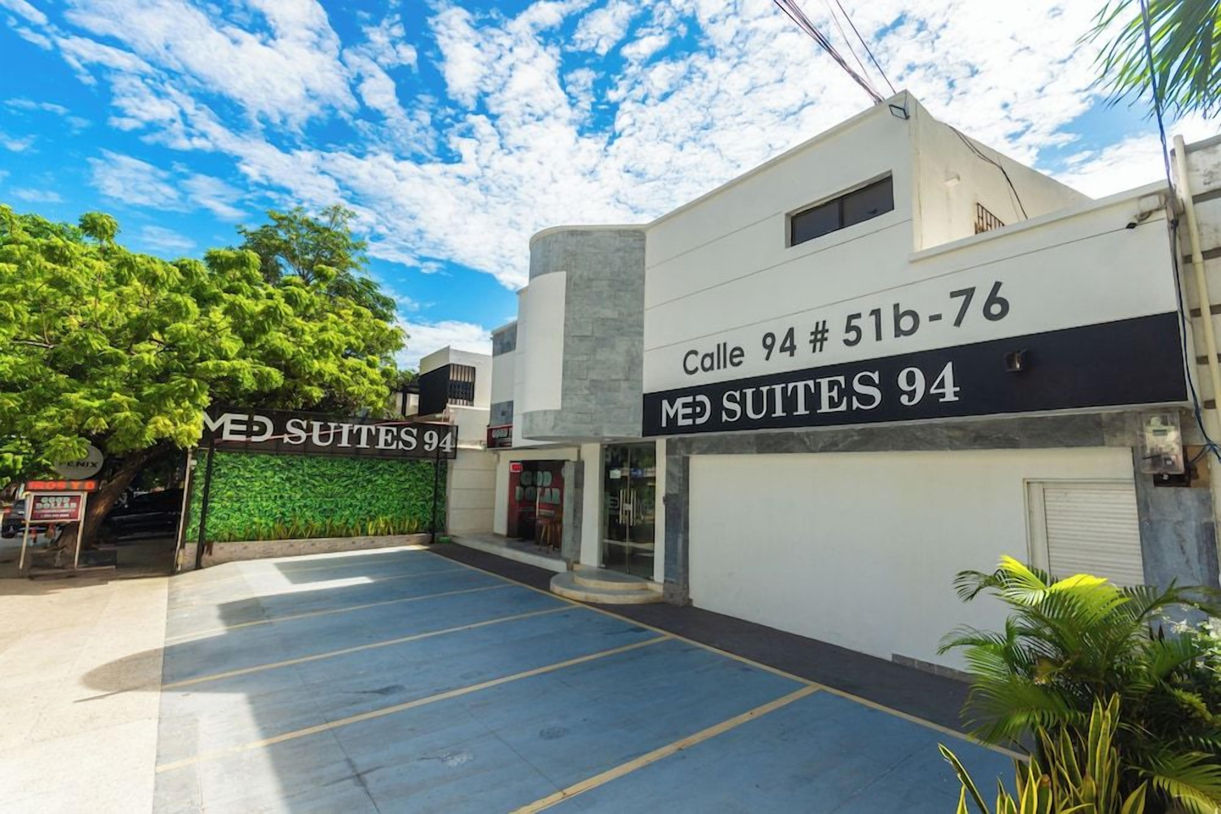 A building with a sign reading 'Calle 94 # 51b-76 MED SUITES 94' and a parking lot in front.