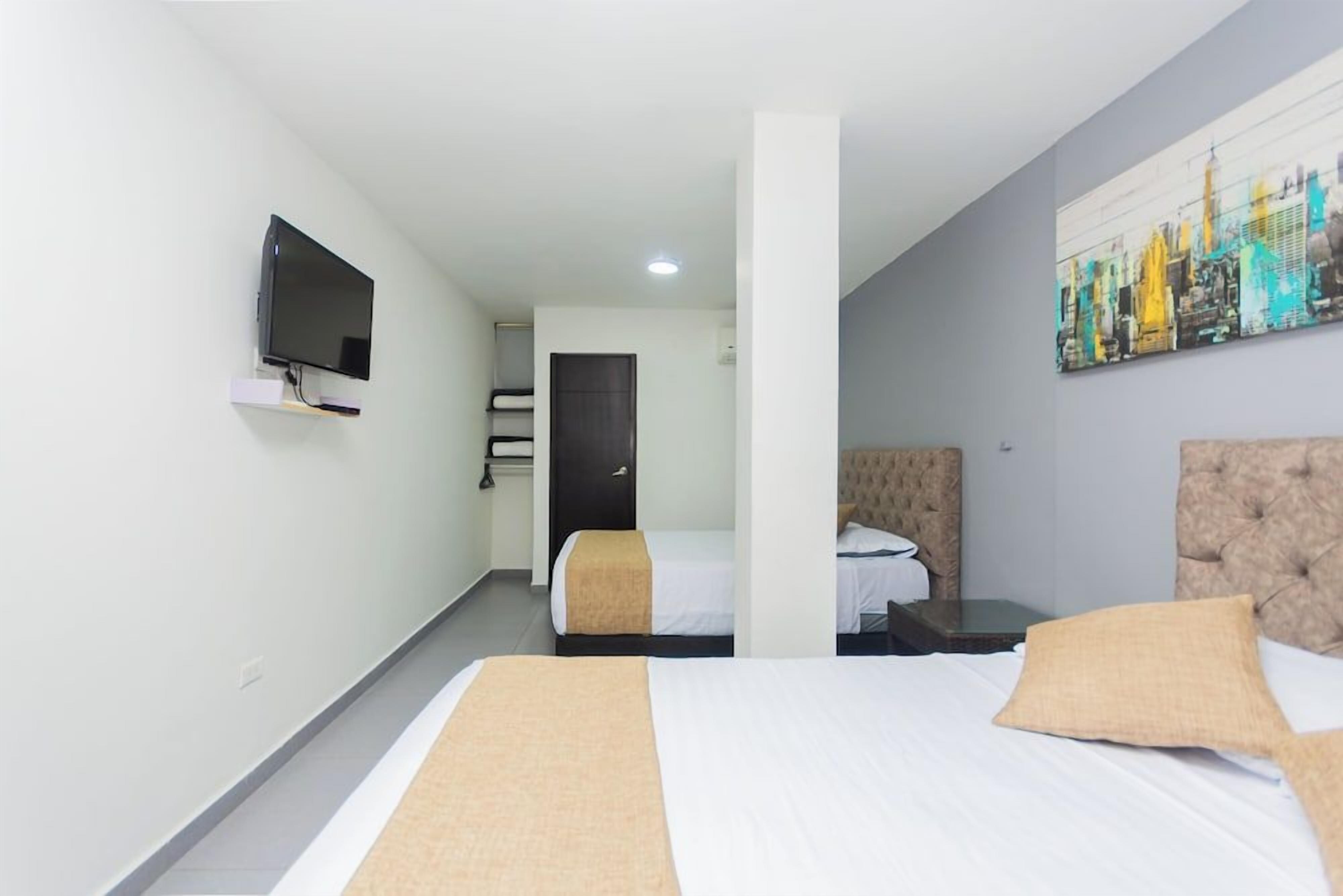 Une chambre d’hôtel avec deux lits, un téléviseur fixé au mur et un tableau représentant un paysage urbain.