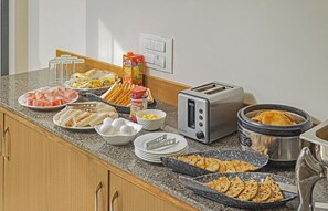 A breakfast buffet with various food items, a toaster, and a slow cooker on a kitchen counter. - Treebo Trend Mall View (Gurugram)