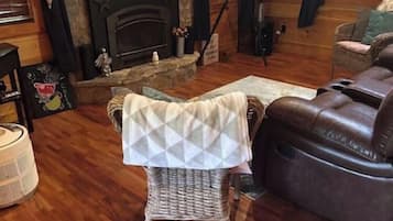 Una sala de estar acogedora con chimenea, un sillón de mimbre con una manta, un sofá de cuero y una pared de piedra.