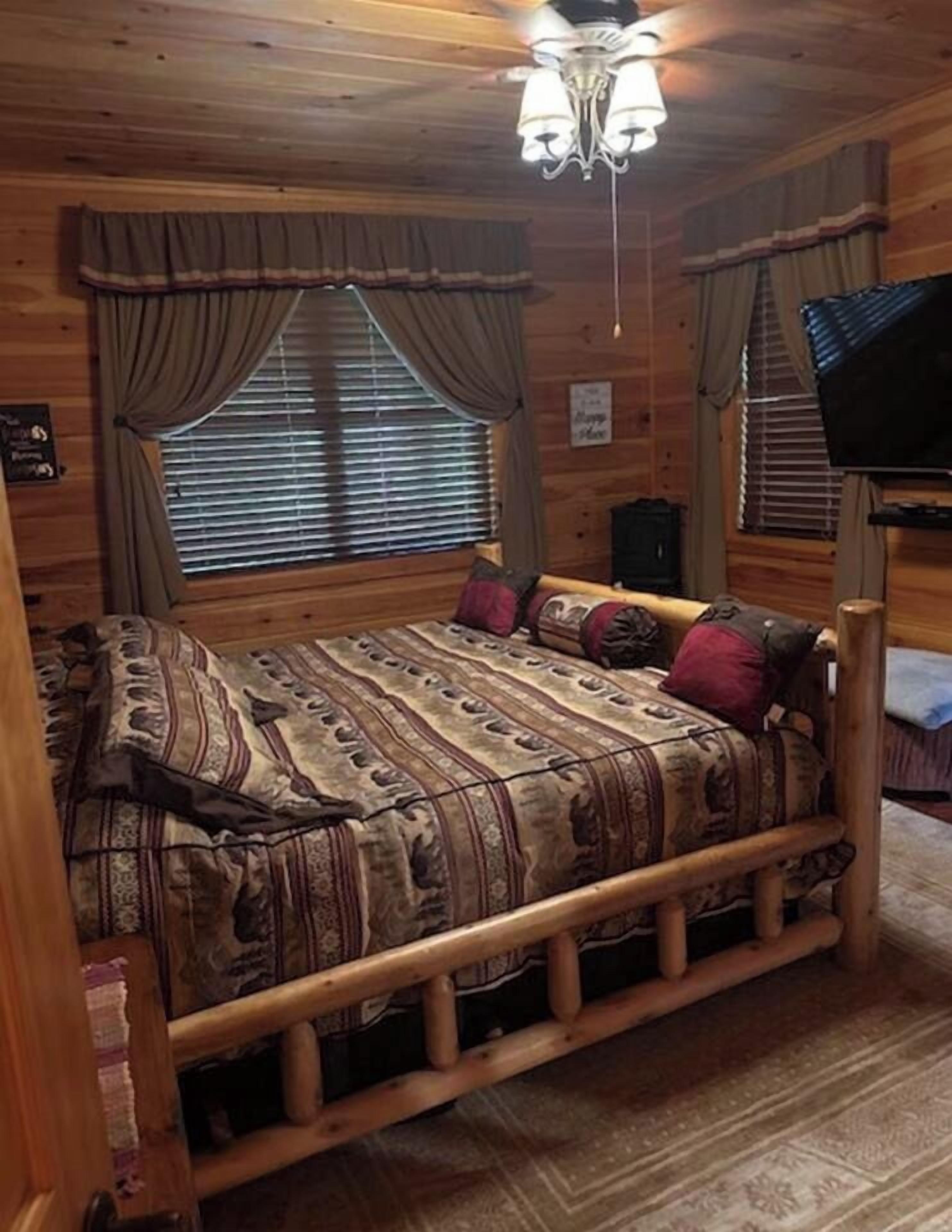 A wooden cabin room with a bed, curtains, and a ceiling fan.