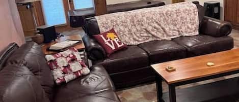 A living room with a brown leather sofa, a wooden coffee table, and a patterned throw blanket.