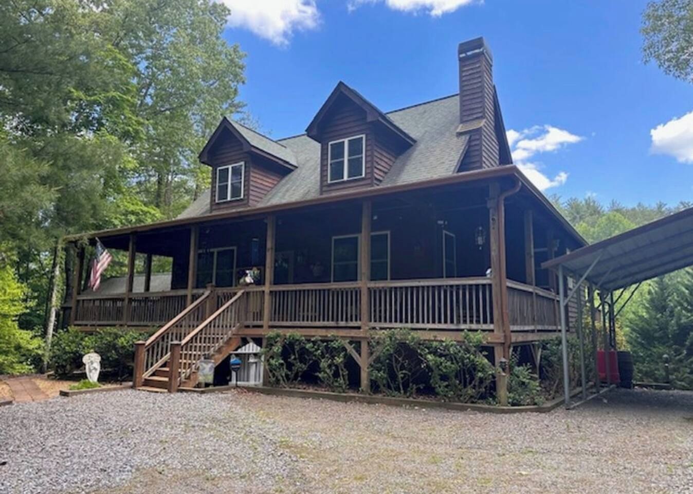 A two-story wooden cabin with a porch, a flag, and a chimney.