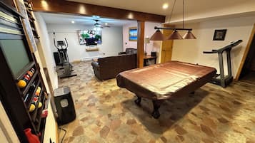 Una habitación con mesa de billar, equipo de ejercicio y televisor.