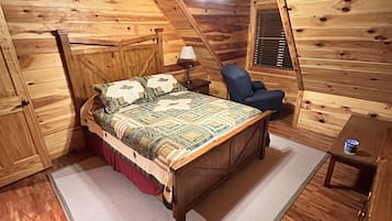 A wooden cabin bedroom with a bed, a chair, a small table, and a ceiling fan.