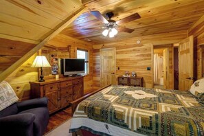Een knus houten chalet slaapkamer met een bed, een televisie, een plafondventilator en een dressoir.