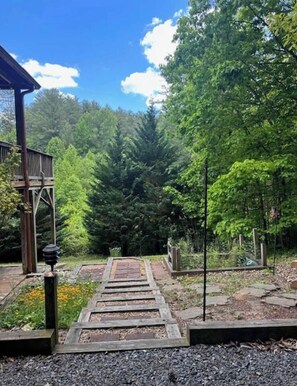 Una terraza de madera que conduce a un área boscosa con un pabellón y un sendero de piedra.