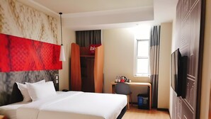A hotel room with a bed, a desk with a chair, a wardrobe, a television, and a window with curtains. - Ibis Hotel (Beijing)