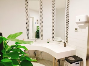 Une salle de bain avec un lavabo blanc, un miroir et un sèche-mains.