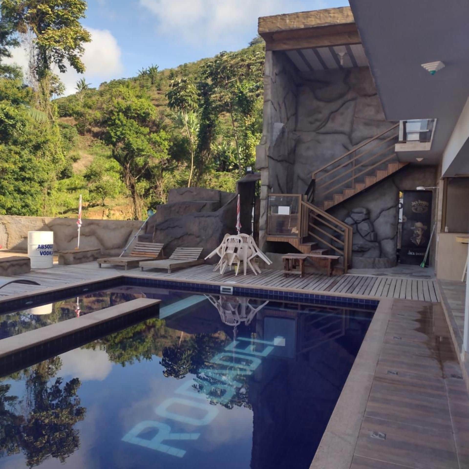 Piscina com parede de pedra, espreguiçadeiras e escadaria que leva a um andar superior.