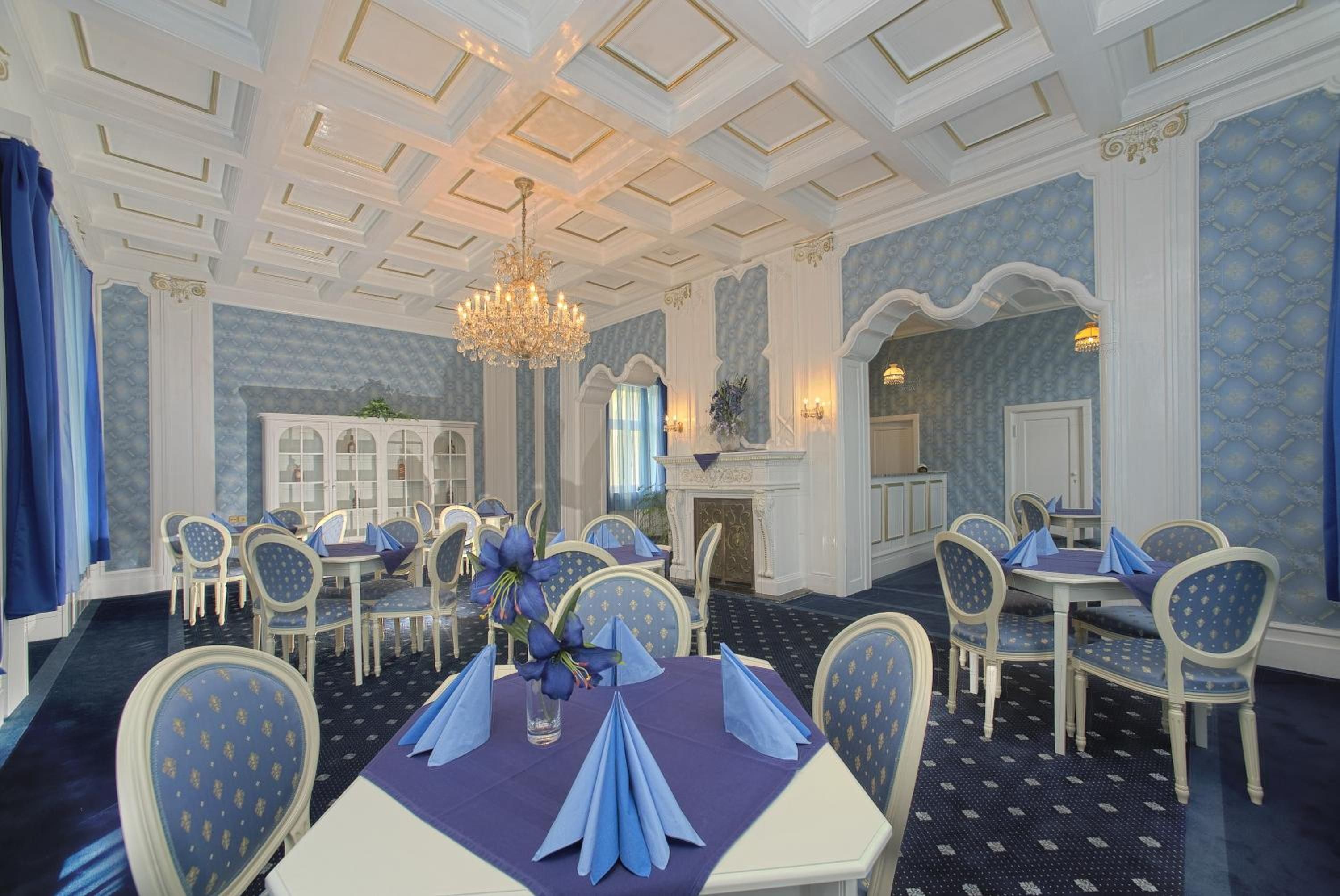 A formal dining room with a chandelier, blue and white decor, and multiple tables set for service.