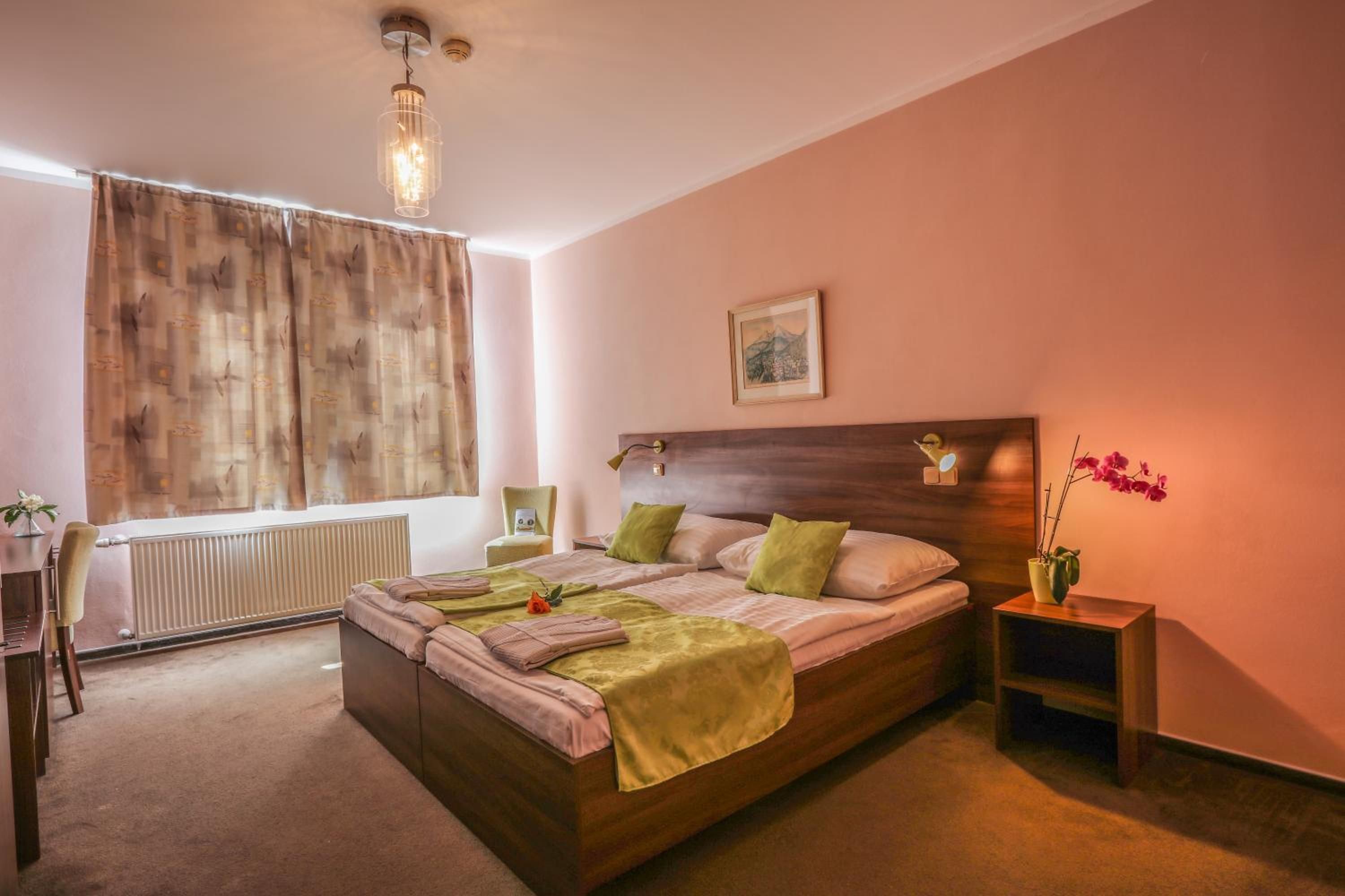 A bedroom with a large bed, a bedside table, a chair, a radiator, and a window with curtains.