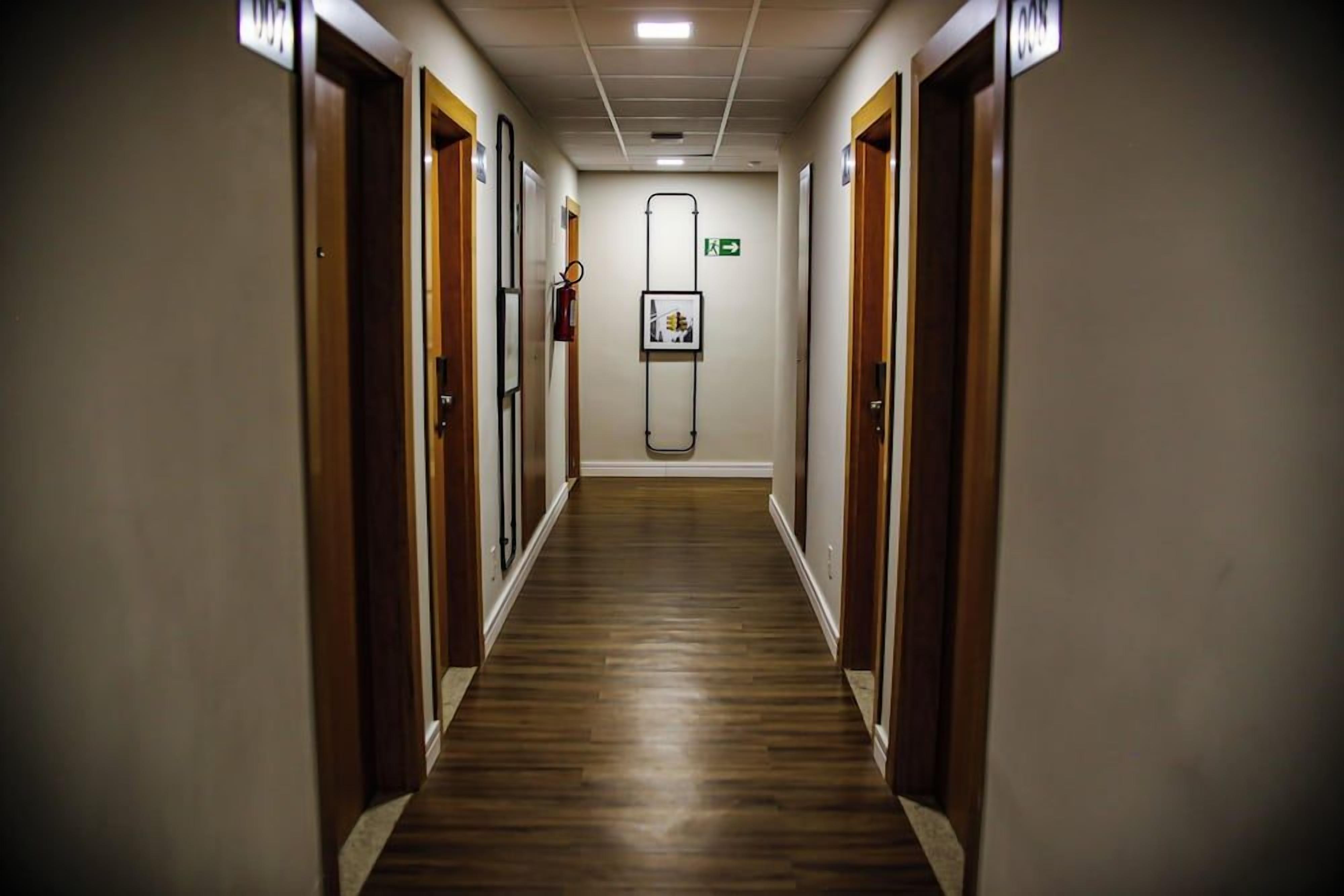 A hotel corridor with wooden flooring, doors on both sides, and a framed picture on the wall.