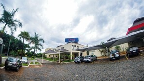 A hotel with a covered parking area, a signboard, and a paved entrance. - Route Hotel Uberaba (Uberaba)