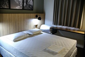 A hotel room with a bed, pillows, a nightstand, a lamp, and a window with curtains.