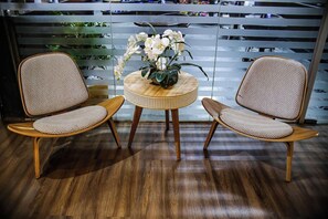 Two wicker chairs with cushioned seats and backs, a small round wooden table with a woven edge, and a potted orchid plant on the table.